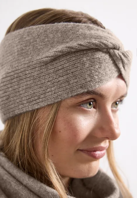 Feinstrick Stirnband in Unifarbe Sandy Mocca Mel. Junge Frau im Profil mit grauem, gestricktem Stirnband und passendem Schal, dezent lächelnd.