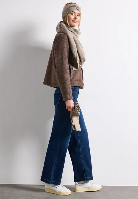 Feinstrick Stirnband in Unifarbe Sandy Mocca Mel. Frau in breiter Jeans, braunem Pullover, Schal und Mütze posiert seitlich vor weißem Hintergrund.