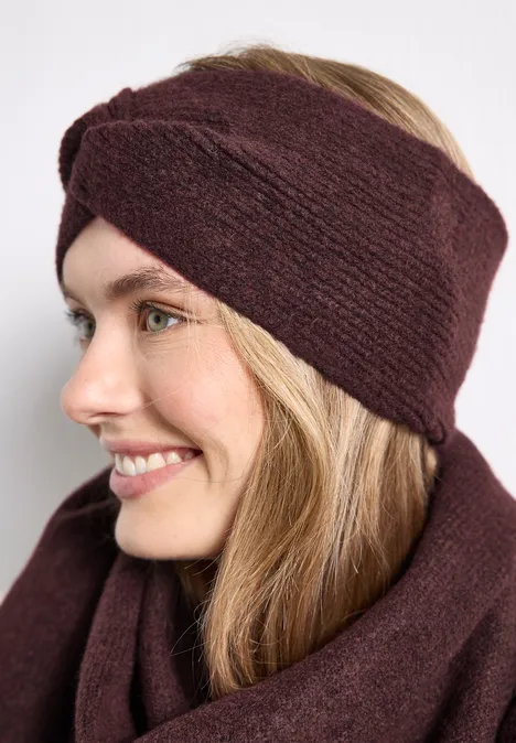 Feinstrick Stirnband in Unifarbe rustic rouge mel. Lächelnde Frau mit gestricktem Haarband und passendem Schal in warmem Dunkelrot.