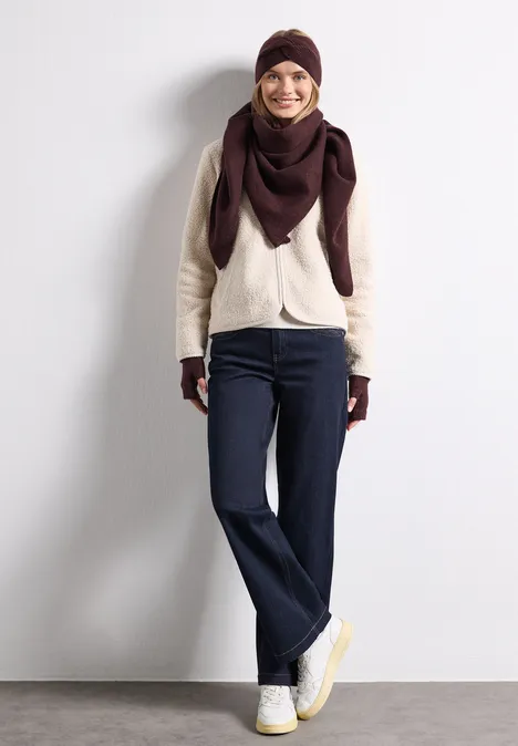 Feinstrick Stirnband in Unifarbe rustic rouge mel. Eine lächelnde Frau in Jeans, weißer Jacke und dunkelrotem Schal lehnt an einer Wand.