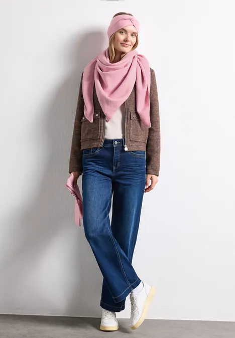 Feinstrick Stirnband in Unifarbe vintage blush mel. Frau mit rosa Mütze und Schal, brauner Jacke, blauen Jeans und weißen Sneakern lehnt lächelnd an einer Wand.