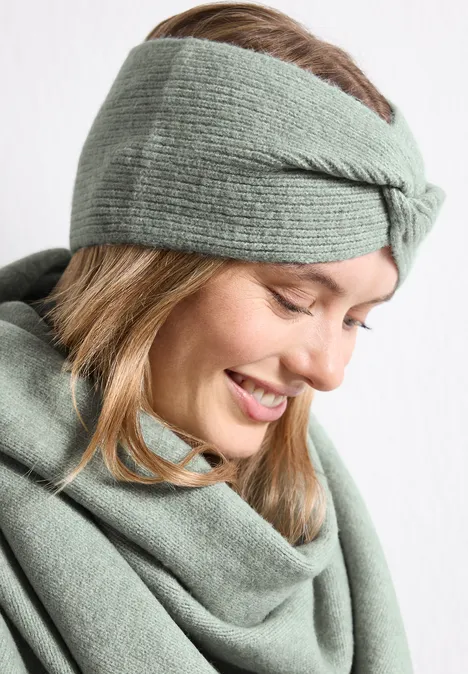 Feinstrick Stirnband in Unifarbe eucalyptus green mel. Frau mit mintgrünem gestrickten Stirnband und Schal lächelt.