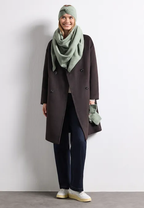 Feinstrick Stirnband in Unifarbe eucalyptus green mel. Frau mit grauem Turban, Schlaufenschal und Handschuhen, dunkelblauem Mantel, blauer Hose und weißen Sneakern.