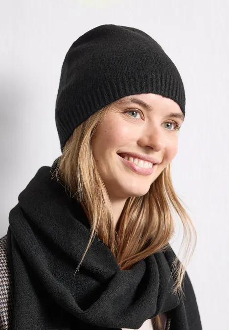 Feinstrick Beanie in Unifarbe Black Eine Frau in schwarzer Mütze und Schal lächelt zur Seite.