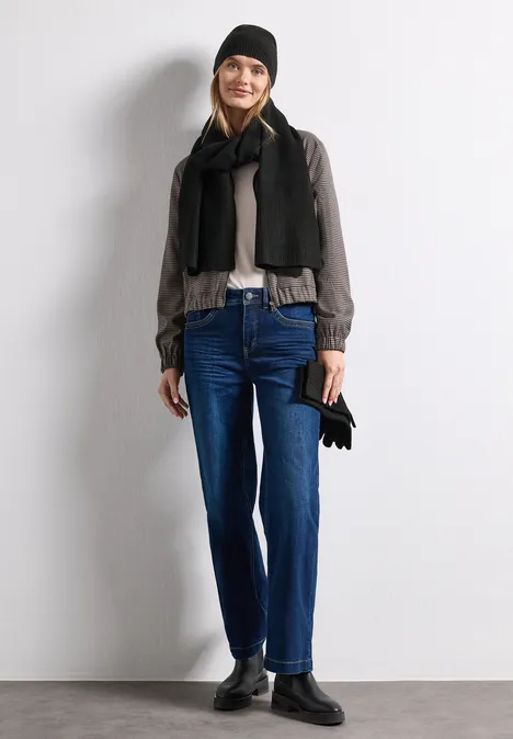Feinstrick Beanie in Unifarbe Black Modische Frau in kaltem Wetter-Outfit: Mütze, Schal, Jacke, Jeans und Stiefel, hält Handschuhe.