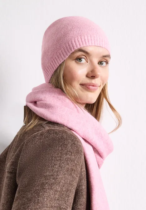 Feinstrick Beanie in Unifarbe vintage blush mel. Eine lächelnde Frau mit rosafarbenem Strickmütze und Schal blickt über die Schulter.