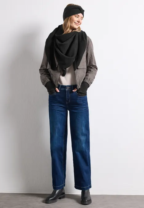 Fijn gebreide driehoekige sjaal in effen kleur Black Vrouw in jeans, grijs jasje, zwarte sjaal en muts, staand voor witte achtergrond, glimlachend.