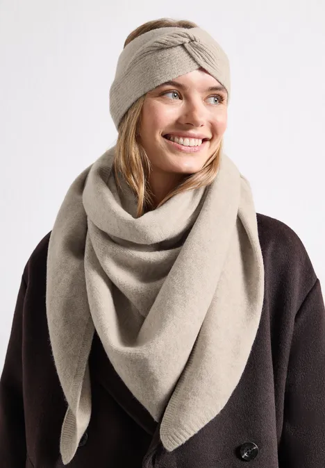 Fijn gebreide driehoekige sjaal in effen kleur Soft Sand Mel. Vrouw met beige gebreide hoofdband en sjaal, donker jasje, lacht