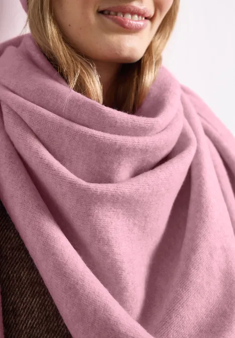 Close-up van een persoon met een zachte, roze wollen sjaal om de hals.