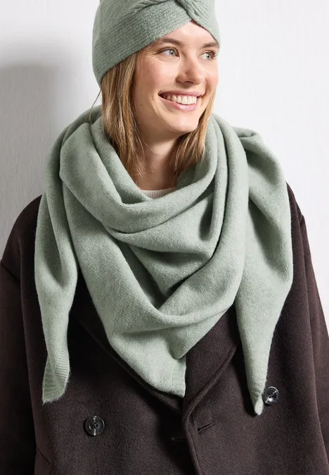 Fijn gebreide driehoekige sjaal in effen kleur eucalyptus green mel. Vrouw in donkerbruine jas met grote pastelgroene driehoekige sjaal en bijpassend turban-achtig haarbandje