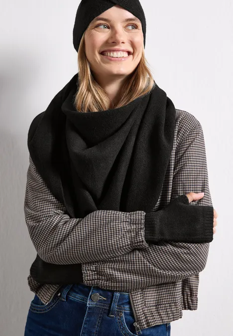 Lächelnde Frau mit schwarzer Mütze, Schal, fingerlosen Handschuhen, kariertem Shirt und Jeans.