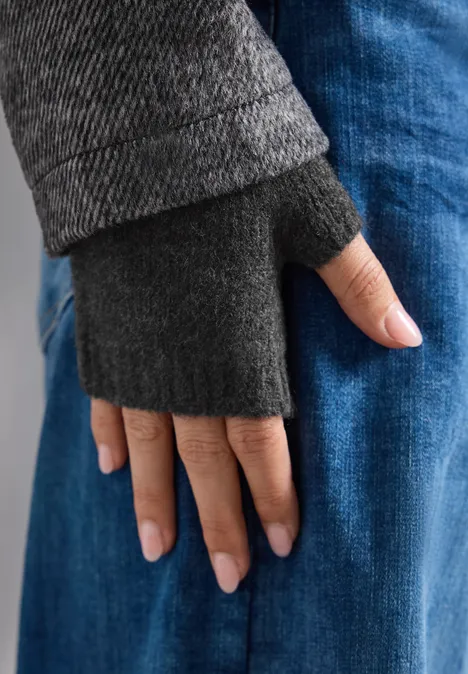Hand in grauem, fingerlosen Handschuh ruht auf blauen Jeans.