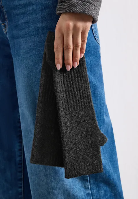 Nahaufnahme einer Hand in Jeans, die einen dunkelgrauen Strick-Handschuh mit Daumenloch hält.