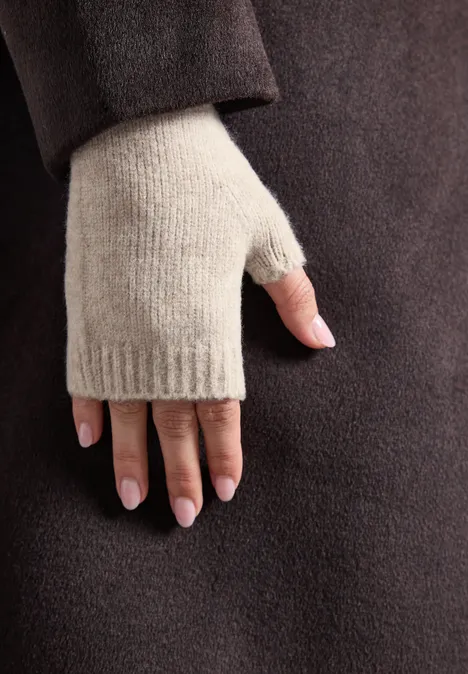 Hand met beige vingerloze want voor een donkerbruine jas.