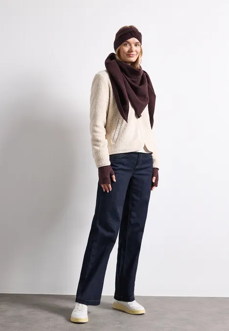 Frau in stylischer Wintermode: heller Pullover, dunkelrote Mütze und Tuch, Handschuhe, dunkle Jeans und weiße Sneaker.