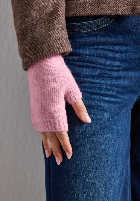 Nahaufnahme einer Person in blauen Jeans und braunem Pullover, die rosa fingerlose Handschuhe trägt.
