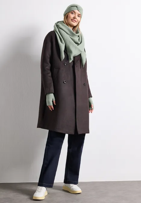 Manchettes en maille fine, couleur unie eucalyptus green mel. Frau in dunkelgrauem Mantel, grüner Mütze, Schal und Handschuhen, dunklen Hosen und weißen Sneakern.
