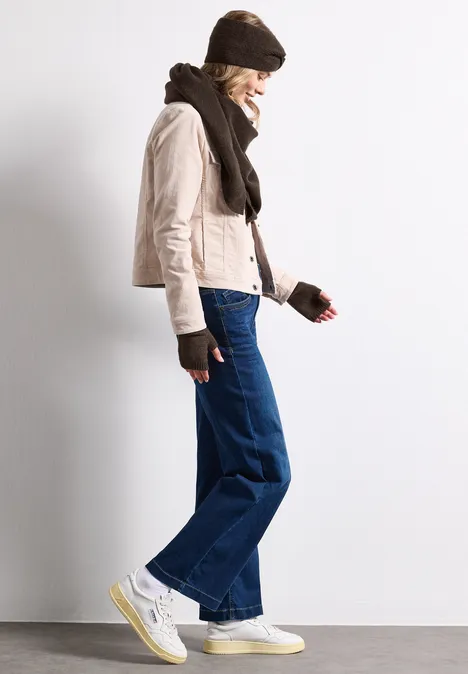 Feinstrick Armwärmer in Unifarbe auburn brown mel. Frau in beiger Jacke, Mütze, Schal, Handschuhen, weiten Jeans und weißen Sneakern seitlich stehend.