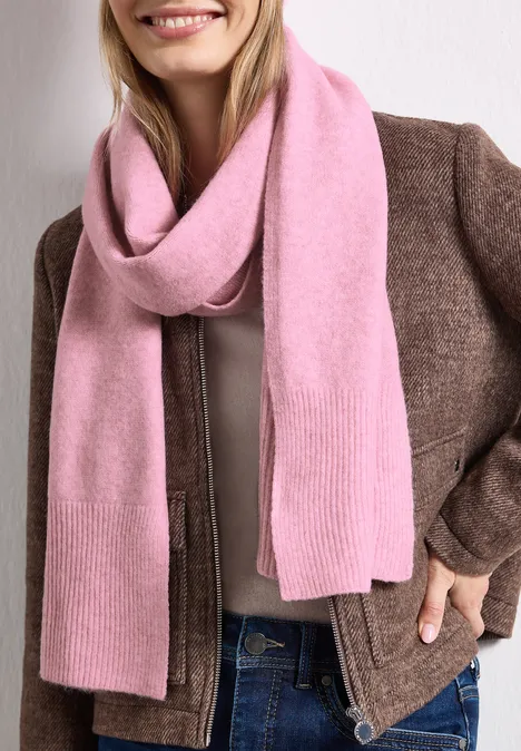 Langer Feinstrickschal in Unifarbe vintage blush mel. Eine lächelnde Frau mit rosafarbenem Schal, brauner Jacke und Jeans.