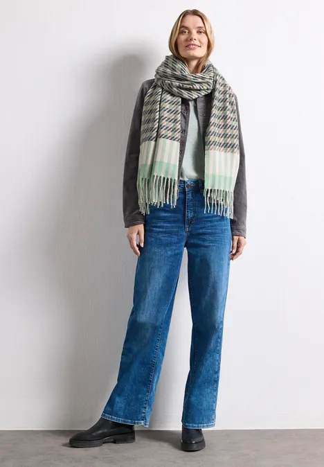 Sjaal met houndstooth-patroon Fresh Sage Vrouw draagt grijze trui, grote geruite sjaal en rechte blauwe jeans, glimlachend.