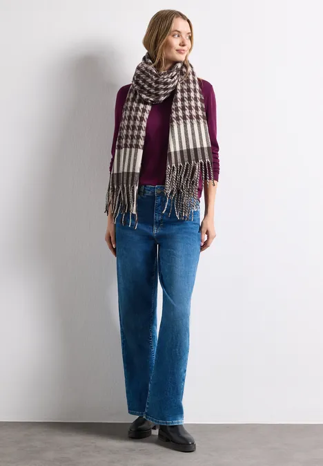 Echarpe à motif pied-de-Poule Muddy Mocha Frau vor weißer Wand mit lila Pullover, kariertem Schal und blauen Jeans, lässig stehend.
