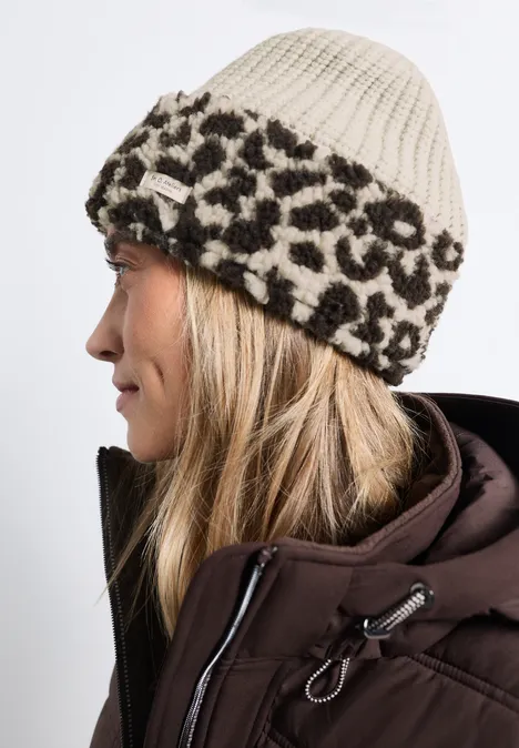 Seitenansicht einer Frau mit beiger Strickmütze mit Leopardenmuster und brauner Winterjacke.