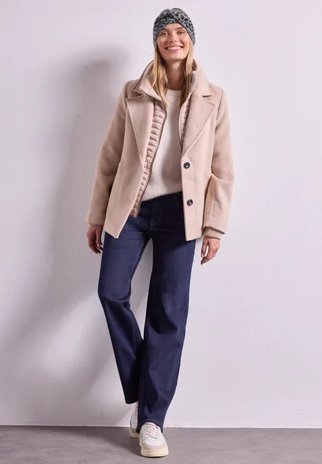 Jacquard Stirnband mit Leo-Muster Black Junge Frau in beiger Jacke, Jeans, Sneakern und Mütze steht lächelnd vor hellem Hintergrund.