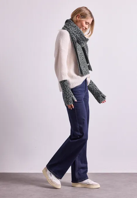 Jacquard Armwärmer mit Leo-Muster Black Eine Frau trägt weißen Pullover, weite Jeans, Schal und Fingerhandschuhe, steht vor hellem Hintergrund.