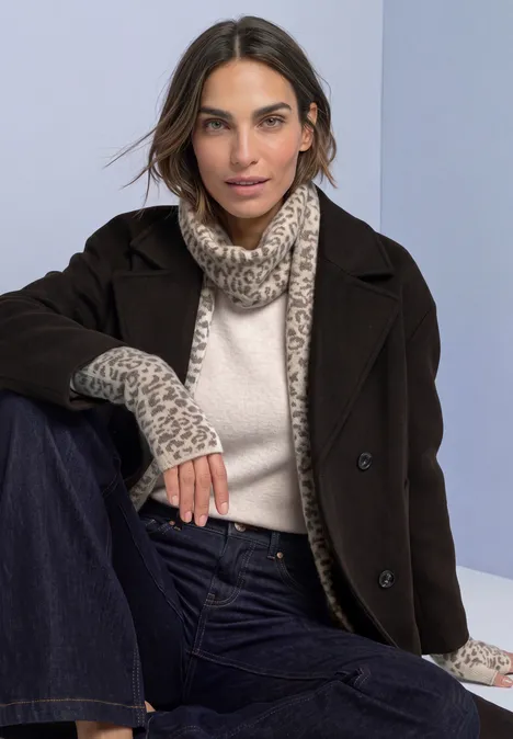 Vrouw in donkerbruine mantel, crèmecoltrui, luipaardsjaal en jeans.