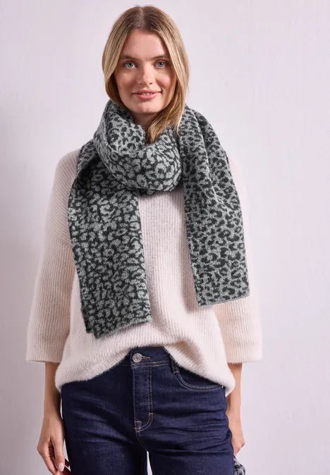 Frau in weißem Pullover, dunkelblauen Jeans und grau-leopardgemustertem Schal.