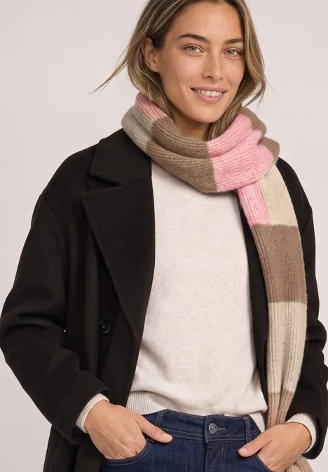 Schal mit Colorblock-Muster warm blush mel. Junge Frau trägt einen Mantel und bunten Schal, lächelt freundlich in die Kamera.