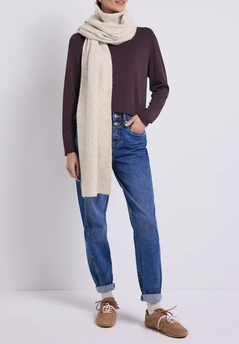 Person trägt dunkles langärmeliges Shirt, beigen Schal, blaue Jeans mit Umschlag und braune Schuhe.