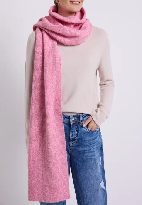 Femme en jean, pull clair et longue écharpe rose.