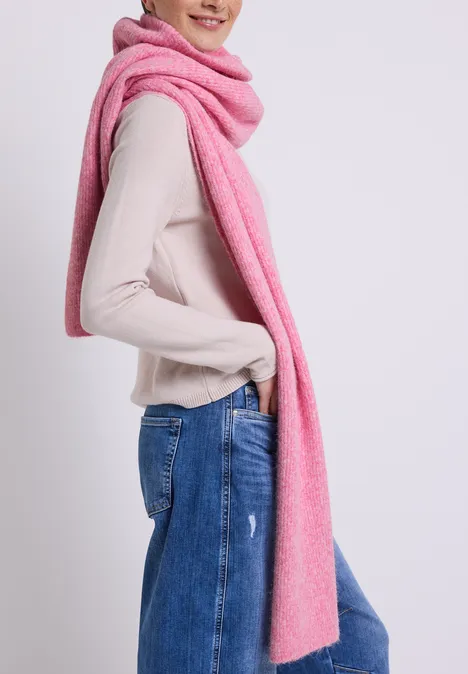Femme portant une longue écharpe rose, un pull beige et un jean bleu.