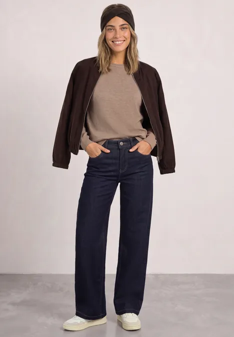 Stirnband in Melange-Optik Black Eine junge Frau in schwarzer Bomberjacke, beigem Pullover, weiten Jeans, hellen Sneakern und Mütze.