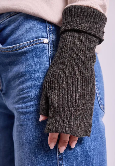 Armwärmer in Melange-Optik Black Gestrickter, dunkelgrauer Fingerhandschuh aus Wolle an einer Hand über blauer Jeans.