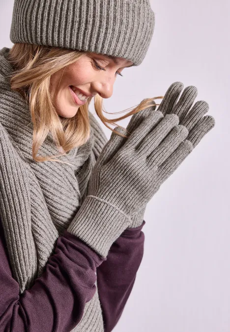 Handschuhe in Melange-Optik Muddy Mocha Frau in grauer Strickmütze, Schal und Handschuhen lächelt und hält ihre Hände zusammen.