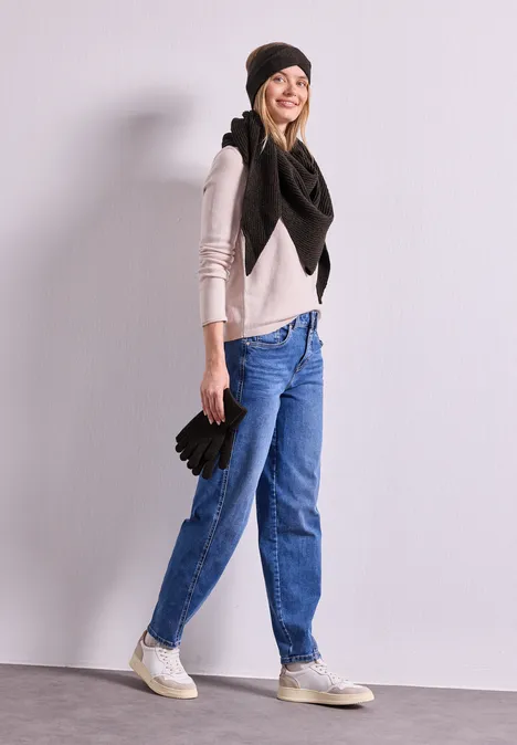 Dreiecksschal in Melange-Optik Black Junge Frau in Jeans, Pullover, großem schwarzem Schal und Mütze hält Handschuhe und lächelt.