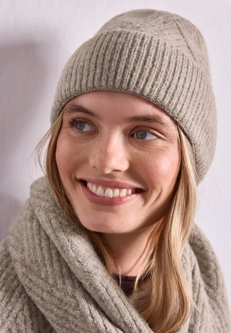Porträt einer lächelnden Frau mit beiger, gestrickter Mütze und passendem Schal.