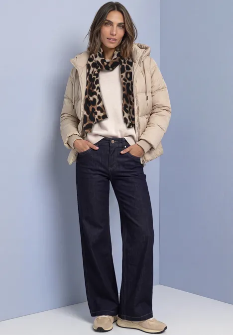 Schal mit Falten und Leo-Muster smooth stone sand Frau in beiger Steppjacke, weißem Pullover, Leopardschal, weiten Jeans und Sneakers vor hellblauem Hintergrund.