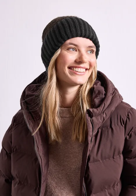 Junge Frau mit schwarzer Mütze und brauner Steppjacke lächelt freundlich.