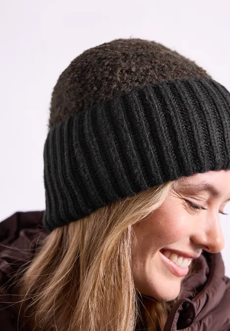 Lächelnde Frau im Profil mit schwarzer Strickmütze und winterlicher Jacke.