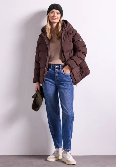 Bouclé-Mix Fäustlinge Black Frau in brauner Steppjacke, Strickmütze, Jeans und Sneakern steht vor weißer Wand.