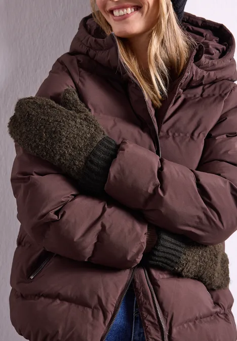 Bouclé-Mix Fäustlinge Black Frau in brauner Daunenjacke und grünen Fäustlingen lächelt und verschränkt die Arme.