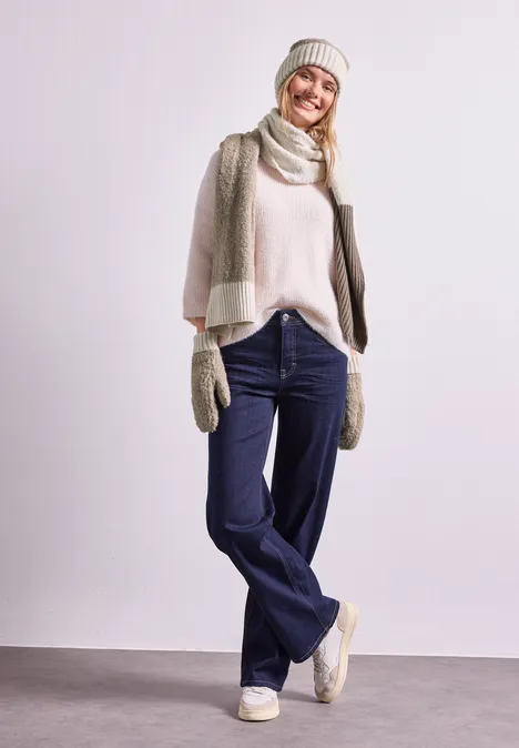 Bouclé-Mix Fäustlinge Muddy Mocha Frau in Winterkleidung mit Mütze, Schal, Handschuhen, hellem Pullover und Jeans vor neutralem Hintergrund.