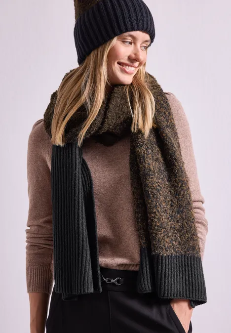 Bouclé-Mix Schal Black Junge Frau mit schwarzer Strickmütze, braunem Pullover und zweifarbiger Strickschal, lächelnd.