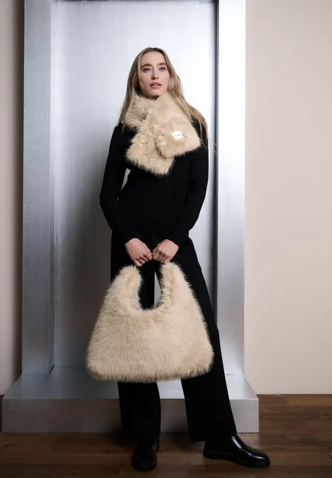 Vrouw in zwarte outfit met een beige, pluizige sjaal en bijpassende tas.