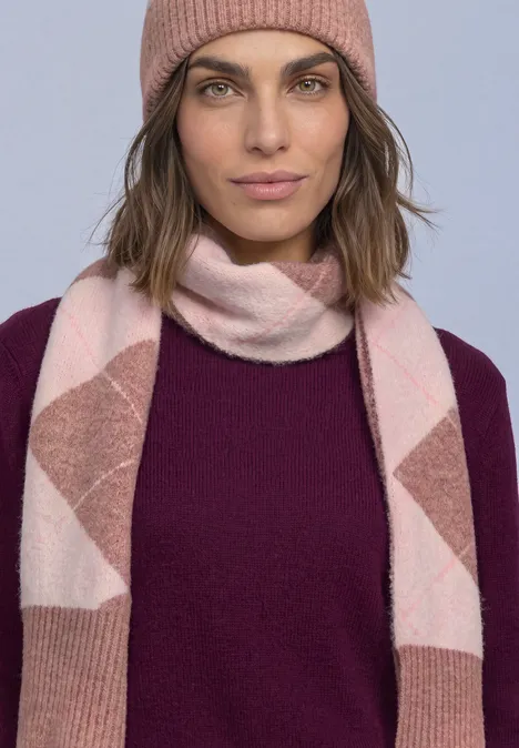Frau mit rosa Beanie, rosa-weiß gemusterter Strickschal und dunkellila Pullover schaut ruhig in die Kamera.