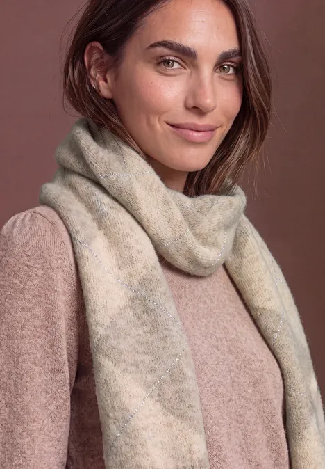 Eine Frau trägt einen weichen, cremefarbenen Schal und einen passenden Pullover, warme neutrale Töne.