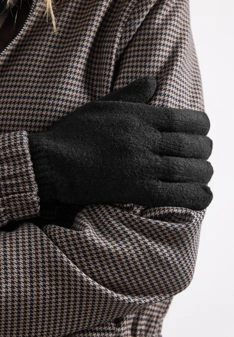 Close-up: persoon in pied-de-poule jas met zwarte handschoenen, armen gekruist voor de borst.
